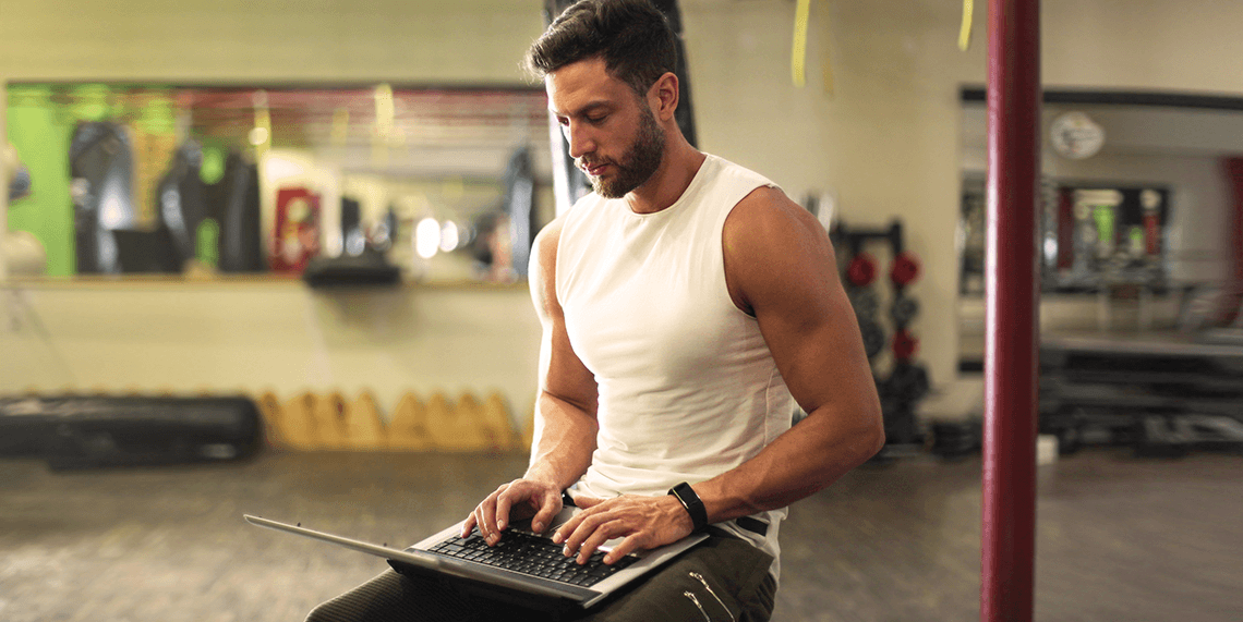 personal-trainer-typing-on-a-laptop-in-an-empty-gym