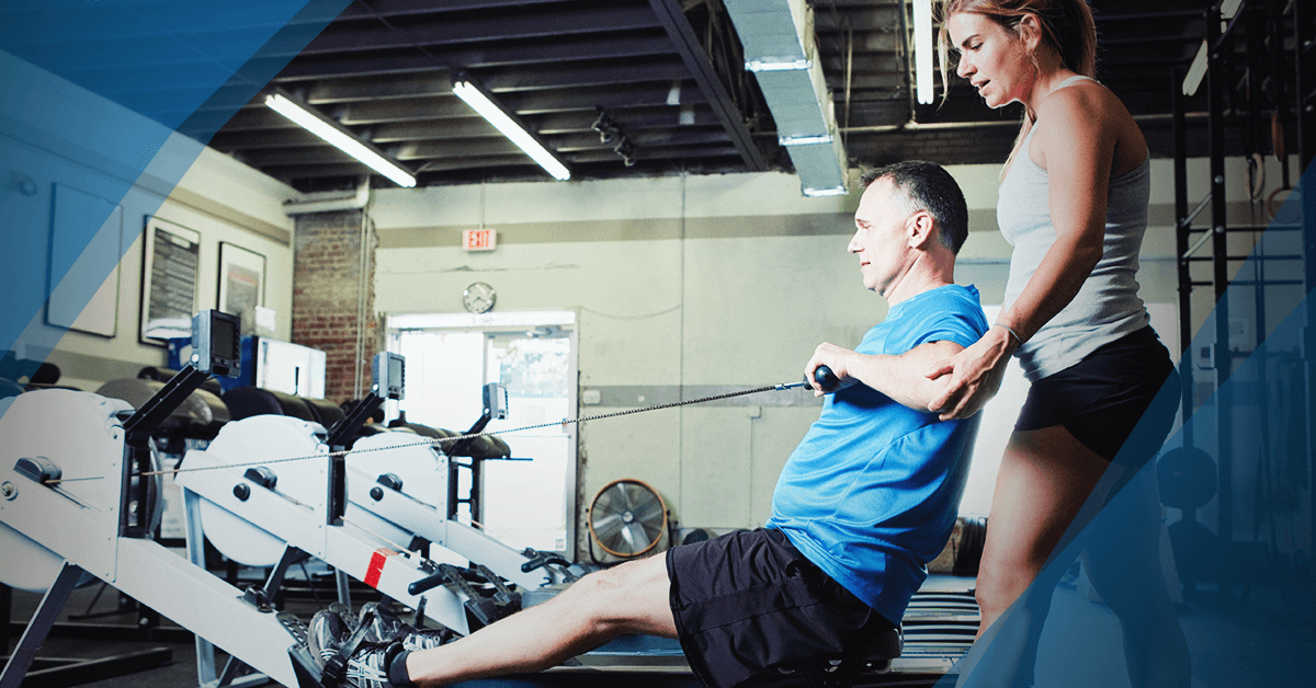 young-trainer-assisting-older-client-on-rowing-maching